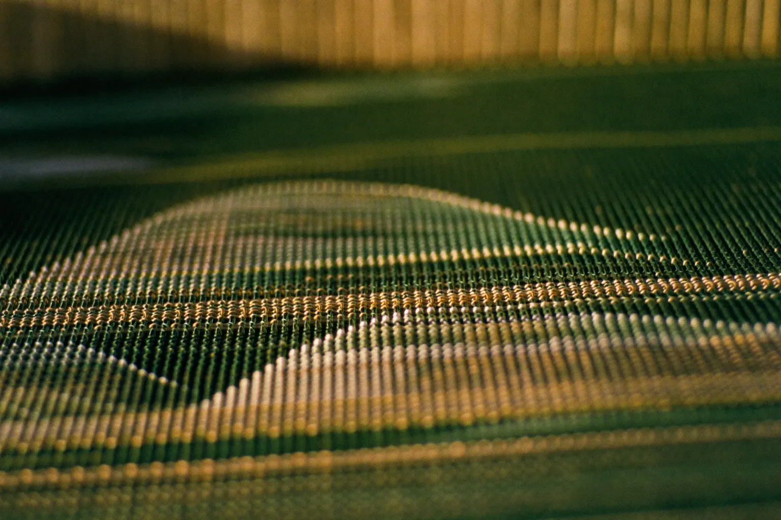 Macro photograph of handwoven kente cloth on the loom: interlaced emerald, gold and ivory threads catching low golden light